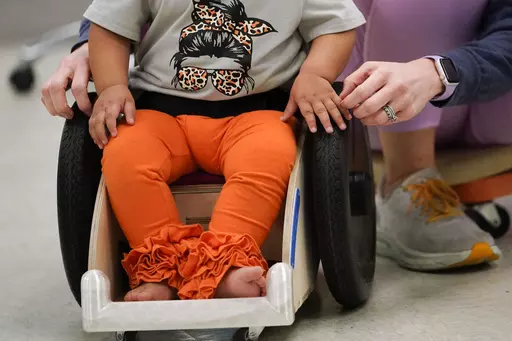 Dr. Jennifer Gaubert, a physical therapist, helps introduce Freya Baudoin,18 months, to her new mobility chair, at the Children's Hospital New Orleans Rehabilitation Center in Metairie, La., Monday, Oct. 30, 2023. Tulane science and engineering students are making the second batch of mobility chairs for toddlers, that will eventually go to pediatric patients at Children's Hospital. Wheelchairs are expensive, and insurance won't cover the cost for children unless the child proves they can operate