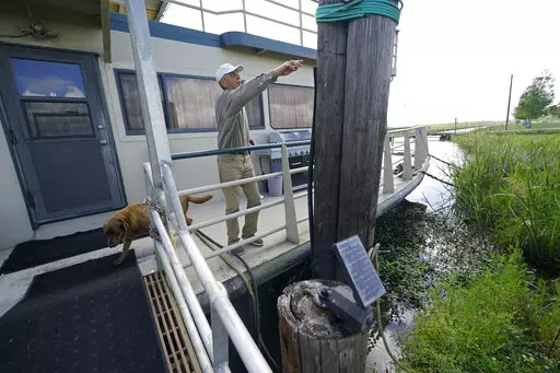 Ted Falgout points out the storm's waterline standing on the houseboat on his property that he rode out Hurricane Ida and has been living in while his home undergoes extensive repairs, in Larose, La., Thursday, April 14, 2022. As climate change increases the threat of hurricanes, cities on the Louisiana coast and Mississippi River are hoping President Biden's $1.2 trillion infrastructure package will provide badly needed funding to fortify locks, levees and other flood protections. (AP Photo/Ger