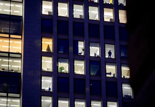 A man looks out of the window of an office building in Frankfurt, Germany, Dec. 6, 2022. A new report says climate commitments by companies aren’t always as green as they seem. The report published Monday, Feb. 13, 2023, concludes that major brands are exaggerating how ambitious their efforts to cut greenhouse gas emissions are, essentially misleading consumers, investors and governments. (AP Photo/Michael Probst, File)