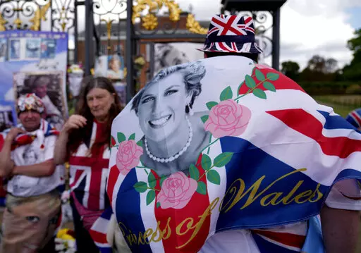 People wave a flag as they stand in front of messages of remembrance for Princess Diana outside the gates of Kensington Palace, in London, Wednesday, Aug. 31, 2022. Wednesday marks the 25th anniversary of Princess Diana's death in a Paris car crash. (AP Photo/Alastair Grant)