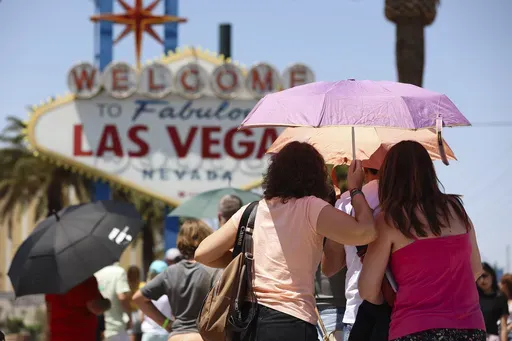 People use umbrellas to block the sun while waiting to take a photo at the "Welcome to Las Vegas" sign July 8, 2024, in Las Vegas. (Wade Vandervort/Las Vegas Sun via AP)