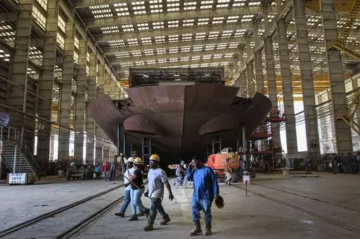 Workers pass the stern of the unfinished 260-foot-long Eco Edison ship in Terrebonne Parish, La., along the Houma Navigation Canal, Monday, April 3, 2023. The ship will serve as a floating housing for U.S. offshore wind technicians and a warehouse for their tools as they operate and maintain wind farms.(AP Photo/Ted Jackson)
