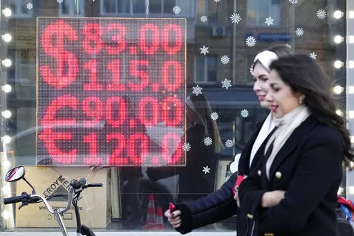 People walk past a currency exchange office screen displaying the exchange rates of U.S. Dollar and Euro to Russian Rubles in Moscow's downtown, Russia, Monday, Feb. 28, 2022.  Moscow’s war on Ukraine and the ferocious financial backlash it’s unleashed are not only inflicting an economic catastrophe on President Vladimir Putin’s Russia. The repercussions are also menacing the global economy and shaking financial markets.  (AP Photo/Pavel Golovkin)