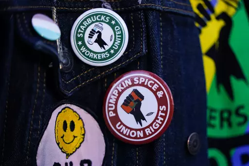 Employee Quint Palermo wears union pins on their jacket as Starbucks workers participate in a walkout and strike during the company's Red Cup Day Thursday, Nov. 16, 2023, at the company's first Reserve roastery in Seattle. The federal government is delaying a new rule that could make it easier for millions of workers to unionize after business groups sued. The National Labor Relations Board says the rule, which was scheduled to go into effect next month, will now be effective Feb. 26 to give it 