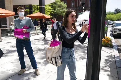 George Washington University student Kai Nilsen, left, watches as American University student Magnolia Mead as they put up posters near the White House promoting student loan debt forgiveness, Friday, April 29, 2022, in Washington. (AP Photo/Evan Vucci)