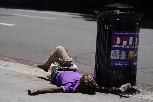 A homeless person lies on the sidewalk while holding a water bottle, Sunday, July 2, 2023, in downtown Los Angeles. Excessive heat warnings remain in place in many areas across the U.S. and are expected to last at least through Monday. (AP Photo/Damian Dovarganes, File)