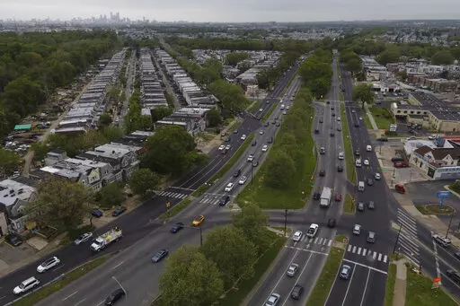 The Philadelphia skyline, top, is seen at a distance as vehicular traffic flows along Roosevelt Boulevard at the intersection with Whitaker Avenue, Thursday, May 12, 2022, in Philadelphia. Roosevelt Boulevard is an almost 14-mile maze of chaotic traffic patterns that passes through some of the city's most diverse neighborhoods and Census tracts with the highest poverty rates. Driving can be dangerous with cars traversing between inner and outer lanes, but biking or walking on the boulevard can b