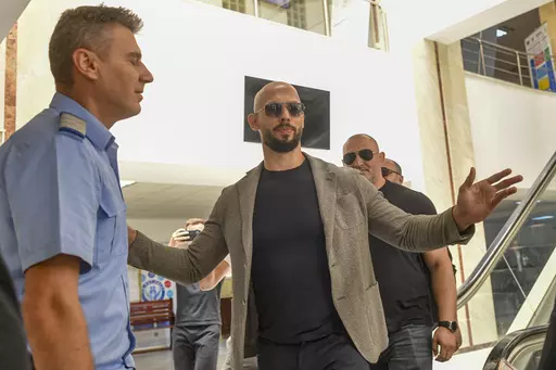 Andrew Tate gestures next to a gendarme as he leaves the Bucharest Tribunal, along with his brother Tristan, right, after the first hearing in their trial, meant to establish if they will remain under house arrest, in Bucharest, Romania, Wednesday, June 21, 2023. Romanian prosecutors charged on Tuesday, June 20, 2023, the Tate brothers and two other suspects with human trafficking, rape and organizing a criminal group for the sexual exploitation of women. (AP Photo/Alexandru Dobre)