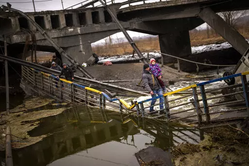 Local militiaman Valery, 37, carries a child as he helps a fleeing family across a bridge destroyed by artillery, on the outskirts of Kyiv, Ukraine, Wednesday, March 2. 2022.  Russian forces have escalated their attacks on crowded cities in what Ukraine's leader called a blatant campaign of terror. (AP Photo/Emilio Morenatti)