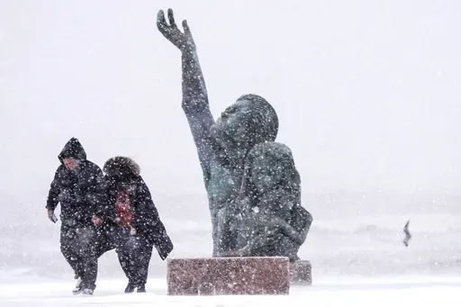 People walk past the 1900 Storm memorial sculpture on Seawall Blvd. during an icy winter storm on Tuesday, Jan. 21, 2025 in Galveston, Texas. (Brett Coomer/Houston Chronicle via AP)