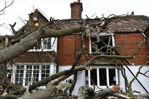 Sven Good, 23, looks out from his bedroom window at the damage caused to the family home a day after a 400-year-old oak tree in the garden was uprooted by Storm Eunice, in Stondon Massey, near Brentwood, Essex, England, Saturday Feb. 19, 2022. Crews cleared fallen trees and worked to restore power to about 400,000 people in Britain as Western Europe cleaned up Saturday after one of the most damaging storms in years. At least 12 people were killed, many by falling trees, in Ireland, Britain, Belg