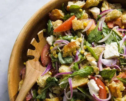This image released by Milk Street shows a recipe for tomato, arugula and bread salad with fresh corn and mozzarella. (Milk Street via AP)
