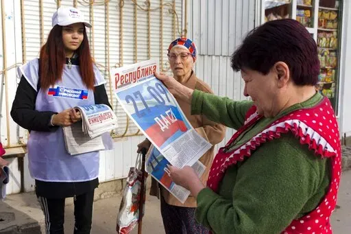 A volunteer of Luhansk regional election commission distributes newspapers to local citizens prior to a referendum in Luhansk, Luhansk People's Republic controlled by Russia-backed separatists, eastern Ukraine, Thursday, Sept. 22, 2022. Authorities in Russian-controlled regions in eastern and southern Ukraine are preparing to hold referendums on becoming part of Russia — a move that could allow Moscow to escalate the war. The votes start Friday in the Luhansk, Kherson and partly Russian-contro