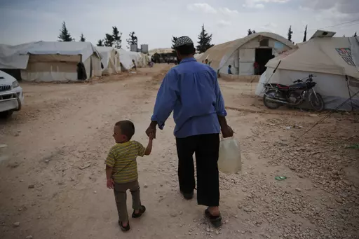 Syrians walk in a camp for internally displaced people in al-Bab, northern Syria, on May 29, 2018. The war in Ukraine helped push the global total of people left internally displaced by conflict or natural disasters to a record high of 71.1 million last year, according to a report released Thursday May 11, 2023. Syria had 6.8 million displaced by conflict after more than a decade of civil war. (AP Photo/Lefteris Pitarakis, File)