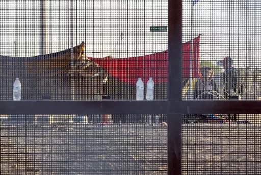 Two migrants, part of a small group, are seeing through the mesh of the border fence as they camp outside a gate in El Paso, Texas, Friday, May 12, 2023. Migrant children in makeshift camps along the U.S.-Mexico border who are waiting to be processed by Border Patrol are in the agency's custody _ something the agency had denied _ and said the Department of Homeland Security must quickly process them and place them in facilities that are “safe and sanitary.”(AP Photo/Andres Leighton, File)