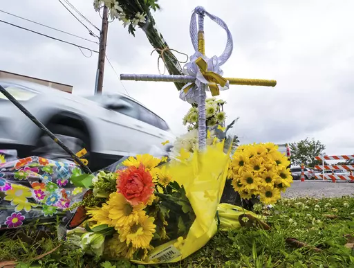 A collection of flowers and a cross with a halo are seen at the location where the body of Linda Frickey was recovered after she was carjacked and dragged to her death a day earlier in New Orleans, March 22, 2022. On Monday, Nov. 20, 2023, three teenage girls facing charges in the dragging death of Frickey pleaded guilty to reduced charges. New Orleans news outlets report that the three — who were charged as adults — were sentenced to 20 years in prison after pleading guilty to attempted man