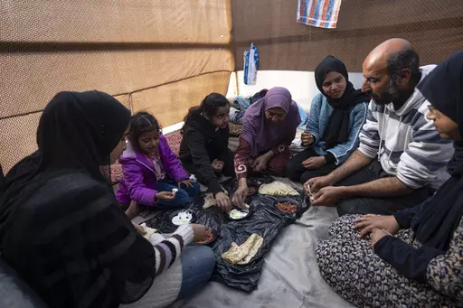 Members of the Abu Jarad family, who were displaced by the Israeli bombardment of the Gaza Strip, eat breakfast at a makeshift tent camp in the Muwasi area, southern Gaza, Monday, Jan. 1, 2024. (AP Photo/Fatima Shbair)