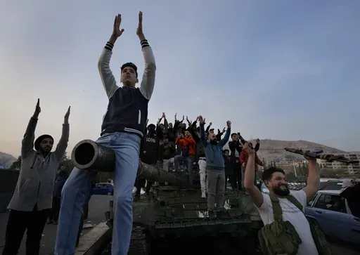 Syrian citizens stand on a government forces tank, that was left on a street, as they are celebrating during the second day of the take over of the city by the insurgents in Damascus, Syria, Monday, Dec. 9, 2024. (AP Photo/Hussein Malla)