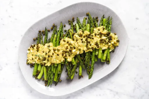 This image released by Milk Street shows a recipe for asparagus covered in Sauce gribiche and fried capers. (Milk Street via AP)
