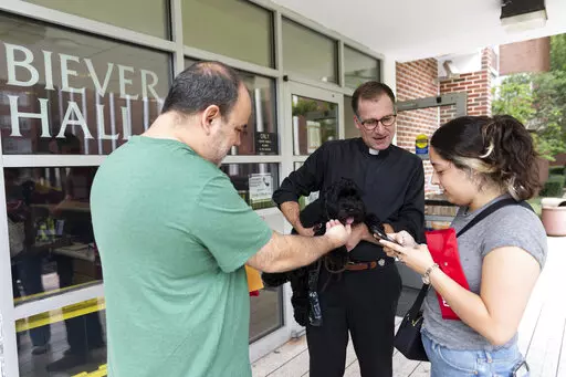 Rev. Justin Daffron, Loyola University New Orleans interim president, and Parleaux, a black cockapoo that is trained as the university's therapy dog, welcome students back to the New Orleans campus, on Aug. 17, 2022. A group blessing of the animals service is scheduled Tuesday evening, Oct. 4, on the lawn next to the university’s church. (Kyle Encar/Loyola University New Orleans via AP)