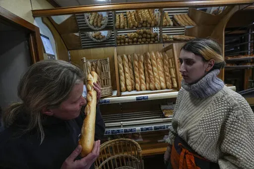 Bakery owner Florence Poirier, LEFT, smells the fresh baguette who comes out of the oven as Mylene Poirier stands next to her at a bakery, in Versailles, west of Paris, Tuesday, Nov. 29, 2022. The humble baguette -- the crunchy ambassador for French baking around the world -- is being added to the U.N.'s list of intangible cultural heritage as a cherished tradition to be preserved by humanity. UNESCO experts gathering Wednesday Nov. 30, 2022 in Morocco decided that the simple French flute deserv