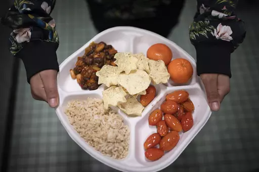 A seventh grader carries her plate which consists of three bean chili, rice, mandarins, cherry tomatoes and baked chips during her lunch break at a public school in the Brooklyn borough of New York on Friday, Feb. 10, 2023. Experts agree that the urgency of climate change and the demands of a surging global population call for an overhaul of how humans get their protein. (AP Photo/Wong Maye-E, File)