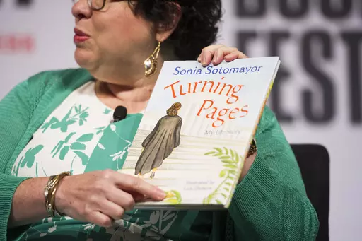 Supreme Court Justice Sonia Sotomayor holds her children's book, "Turning Pages: My Life Story", while speaking to an audience at the Library of Congress National Book Festival in Washington, Sept. 1, 2018. (AP Photo/Cliff Owen, File)
