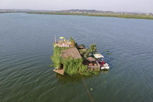 A floating restaurant and bar is seen from the air in Lake Victoria near the Luzira area of Kampala, Uganda Saturday, Feb. 18, 2023. Flowering plants rise from the water into the wooden hull of James Kateeba's boat, used as a floating restaurant and bar that can be unmoored to drift for pleasure, but the greenery emerges from an innovative recycling project which uses thousands of dirt-encrusted plastic bottles to anchor the boat. (AP Photo/Patrick Onen)