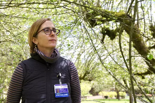 Rev. Jo Laurence, a Buddhist chaplain, poses for a photo on April 22, 2022 in the garden of a memory care facility in Portland, Ore. before visiting hospice patients to offer spiritual care. Buddhist chaplains like Laurence have become more numerous in hospitals, hospices, and prisons and graduate programs to train them have proliferated across the country. (AP Photo/Gosia Wozniacka) Rev. Jo Laurence, a Buddhist chaplain, speaks about meditation and bodily suffering with hospice patient Skylar F