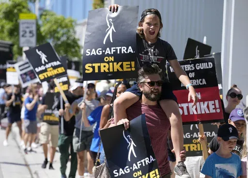 Director of Photography Jac Cheairs and his son, actor Wyatt Cheairs, 11, take part in a rally by striking writers and actors outside Netflix studio in Los Angeles on Friday, July 14, 2023. (AP Photo/Chris Pizzello, File)