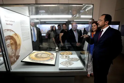 Cyprus' President Nikos Christodoulides, right, stands in front of an Orthodox Christian icon after the same was repatriated and displayed at the Archeological museum in capital Nicosia, Cyprus, Monday, July 22, 2024. The returned artifacts numbering around 60, including jewelry from the Chalcolithic Period dating between 3500-1500 BC, Bronze Age bird-shaped idols, jars and spearheads as well as many Orthodox Christian icons were part of a larger haul of 250 antiquities that German authorities h