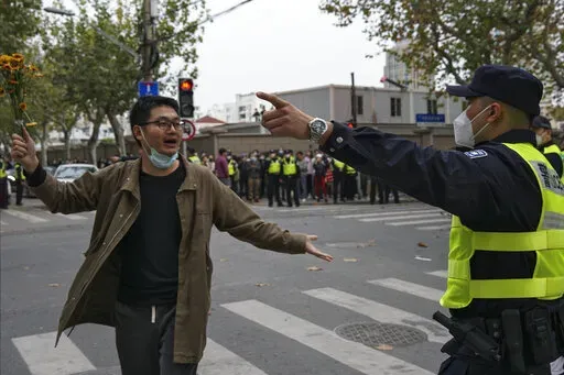 A protester holding flowers is confronted by a policeman during a protest on a street in Shanghai, China on Nov. 27, 2022. What started as an unplanned vigil last weekend in Shanghai by fewer than a dozen people grew hours later into a rowdy crowd of hundreds. The protesters expressed anger over China's harsh COVID-19 policies that they believed played a role in the deadly fire on Nov. 24 in a city in the far west. (AP Photo, File)