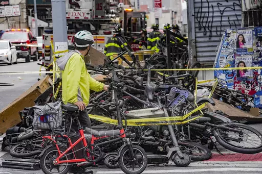 A biker stops to look at a pile of e-bikes in the aftermath of a fire in Chinatown, which authorities say started at an e-bike shop and spread to upper-floor apartments, Tuesday June 20, 2023, in New York. New York City is receiving $25 million in emergency funding from the U.S. Department of Transportation to establish scores of new e-bike charging stations across the city. Mayor Eric Adams announced the funding Sunday, June 25. (AP Photo/Bebeto Matthews, File)