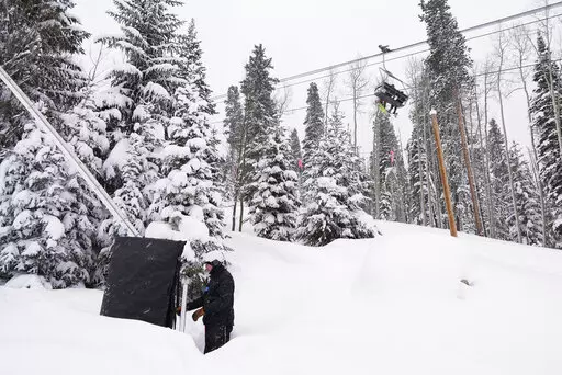 Ian Sidwell adjusts a machine used to make snow at Vail Mountain Resort as snowboarders ride a lift, Wednesday, Dec. 29, 2021, in Vail, Colo. Newer snowmaking technology is allowing ski areas to be more efficient with energy and water usage as climate change continues to threaten snowpack levels. (AP Photo/Brittany Peterson)