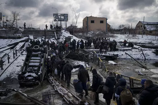 Ukrainians cross an improvised path under a destroyed bridge while fleeing Irpin, in the outskirts of Kyiv, Ukraine, Tuesday, March 8, 2022. As milestones go, the first anniversary of Russia's invasion of Ukraine is both grim and vexing. It marks a full year of killing, destruction, loss and pain felt even beyond the borders of Russia and Ukraine. (AP Photo/Felipe Dana, File)