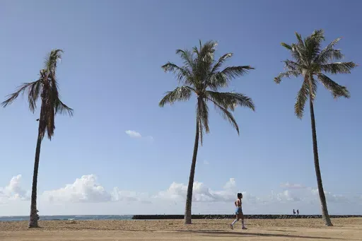A beachgoer walks down Waikiki Beach, Thursday, Oct. 15, 2020, in Honolulu. About two years after 13 children and teens in Hawaii sued the state over the threat posed by climate change, both sides reached a settlement that includes an ambitious requirement to decarbonize Hawaii’s transportation system in the next 21 years. (AP Photo/Marco Garcia, File)