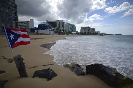 A Puerto Rican flag flies on an empty beach at Ocean Park, in San Juan, Puerto Rico, Thursday, May 21, 2020.  Puerto Rico’s nearly five-year bankruptcy battle was resolved Tuesday, Jan. 18, 2022, after a federal judge signed a plan that slashes the U.S. territory’s public debt load as part of a restructuring and allows the government to start repaying creditors. (AP Photo/Carlos Giusti, File)
