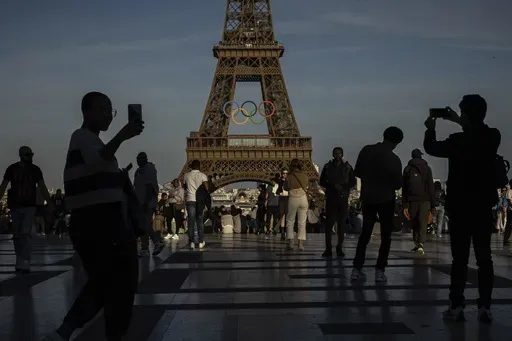 People use their smartphones near the Olympic rings that are displayed on the Eiffel Tower in Paris, June 7, 2024 in Paris. Cybersecurity experts and French officials say Russian disinformation campaigns against France are zeroing in on legislative elections and the Olympic Games which open in Paris at the end of the month. (AP Photo/Aurelien Morissard, File)