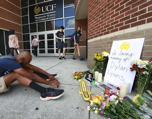 A person sits in front of the pop-up memorial for slain Spectrum News 13 journalist Dylan Lyons at the University of Central Florida Nicholson School of Communications in Orlando, Fla., Thursday, Feb. 23, 2023. Lyons, a graduate of UCF, was shot and killed while covering a homicide in Orlando on Wednesday. (Joe Burbank /Orlando Sentinel via AP)