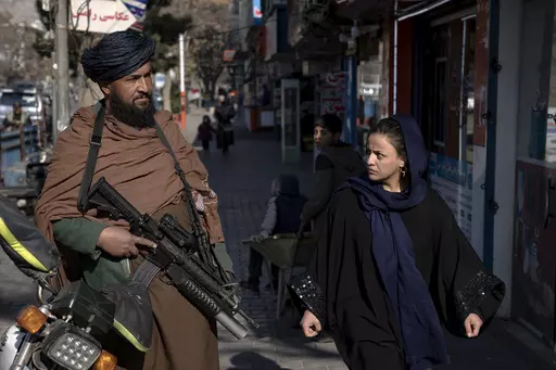A Taliban fighter stands guard as a woman walks past in Kabul, Afghanistan, on Dec. 26, 2022. The United Nations' human rights chief on Tuesday Dec. 27, 2022. A U.N. report on Monday, May 8, 2023 condemned the Taliban for their harsh rule since seizing power in Afghanistan — including public execution, lashings, and amputations — and for ignoring international calls to respect human rights and freedoms. (AP Photo/Ebrahim Noroozi, File)