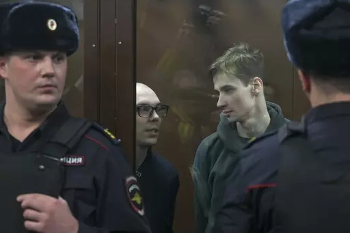 Artyom Kamardin, left, and Yegor Shtovba, right, stand behind a glass in a cage in a courtroom in Moscow, Russia, Thursday, Dec. 28, 2023. Artyom Kamardin was given a 7-year prison sentence Thursday for reciting verses against Russia's war in Ukraine, a tough punishment that comes during a relentless Kremlin crackdown on dissent. Yegor Shtovba, who participated in the event and recited Kamardin's verses, was sentenced to 5 1/2 years on the same charges. (AP Photo, File)