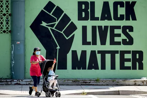 A girl in a stroller plays with a squirt gun as a woman pushes her past a Black Lives Matter mural in the Shaw neighborhood in Washington, Monday, July 13, 2020. The National Urban League released its annual report on the State of Black America on Tuesday, April 12, 2022, and its findings are grim. This year’s Equality Index shows Black people still get only 73.9 percent of the American pie white people enjoy.  (AP Photo/Andrew Harnik, File)