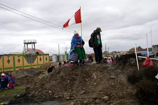An Aymara woman, holding a Peruvian national, stands on a pile of dirt serving as a roadblock set up by anti-government protesters, in Acora, southern Peru, Jan. 29, 2023. Peruvians have been protesting since early December, when former President Pedro Castillo was impeached after a failed attempt to dissolve Congress. His vice president, Boluarte, immediately took over — and has faced strong opposition ever since. (AP Photo/Rodrigo Abd, File)