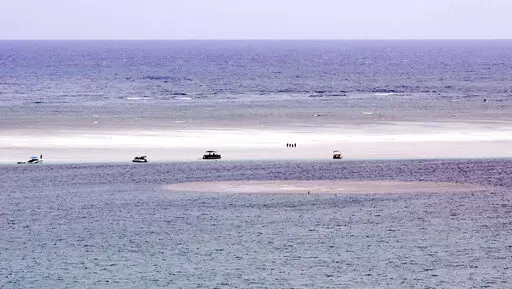 FILE — In this Aug. 15, 2015, file photo, people stand on the sandbar in Hawaii's Kaneohe Bay. Hawaii's Department of Land and Natural Resources is warning people that they face arrest if found burning Christmas trees at an oceanic sandbar. The sandbar found between the open Pacific Ocean and Kaneohe Bay on Oahu's windward side is a popular gathering place for local boaters and tourists. A tradition of piling up Christmas trees for bonfires on the sandbar is harming the environment, officials 