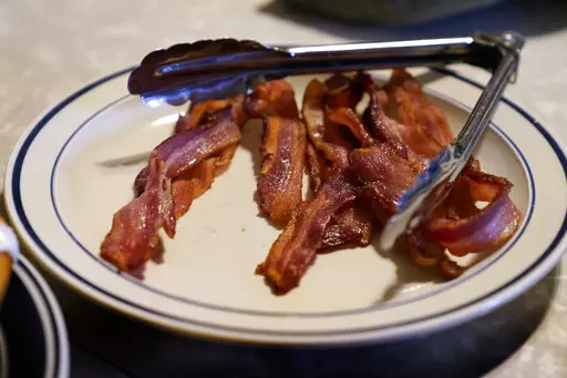 FILE - A plate of bacon sits on the kitchen table on the Ron Mardesen farm, Thursday, Dec. 2, 2021, near Elliott, Iowa. A 2018 voter-approved California ballot measure, to take effect, Jan. 1, 2022, set the nation's toughest living space standards for breeding pigs. Critics have called for putting off enforcement until 2024 for fear prices will rise and jobs will be lost. Mardesen already meets the California standards for the hogs he sells to specialty meat company Niman Ranch, which supported 