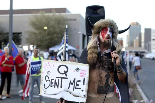 Jacob Anthony Chansley, who also goes by the name Jake Angeli, a Qanon believer speaks to a crowd of President Donald Trump supporters outside of the Maricopa County Recorder's Office where votes in the general election are being counted, in Phoenix on Nov. 5, 2020. From the Salem witch trials to fears of the Illuminati to the Red Scare to QAnon, conspiracy theories have always served as dark counter programming to the American story taught in history books. (AP Photo/Dario Lopez-Mills, File)