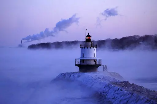 Spring Point Ledge Light is surrounded by arctic sea smoke while emissions from the Wyman Power plant, background, are blown horizontal by the fierce wind, Saturday, Feb. 4, 2023, in South Portland, Maine. The morning temperature was about -10 degrees Fahrenheit. (AP Photo/Robert F. Bukaty)