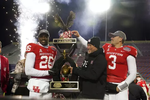 CORRECTS TO ART GREEN NOT MOSES ALEXANDER - Houston head coach Dana Holgorsen, center, looks on as he and defensive back Art Green (26) and quarterback Clayton Tune (3) hoist the Independence Bowl championship trophy following their win over Louisiana-Lafayette in an NCAA college football game Friday, Dec. 23, 2022, in Shreveport, La. (AP Photo/Rogelio V. Solis)
