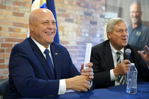 White House senior adviser Mitch Landrieu, left, smiles as U.S. Agriculture Sec. Tom Vilsack  speaks in a repurposed railroad depot in Elm City, N.C., during an event to announce rural broadband funding on Thursday, Oct. 27, 2022. AccessOn Networks will receive $17.5 million to connect communities, businesses, farms and educational facilities to high-speed internet. (AP Photo/Allen G. Breed)