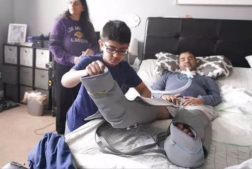 Ronan Kotiya, 11, removes a compression leg sleeve from his father Rupesh Kotiya as his mother Siobhan Pandya looks at their home in Plano, Texas, Sunday, April 10, 2022. Ronan helps care for his father who suffers from ALS and is dependent on a ventilator and around the clock care. Millions of Americans with serious health problems depend on children ages 18 and younger to provide some or all of their care at home. An exact number is hard to pin down, but researchers think millions of children 